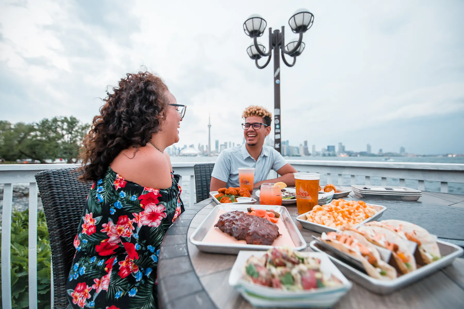 Toronto Island BBQ Beer Co. patio people sharing meal distant CN Tower daytime Food Drink Nightlife Image