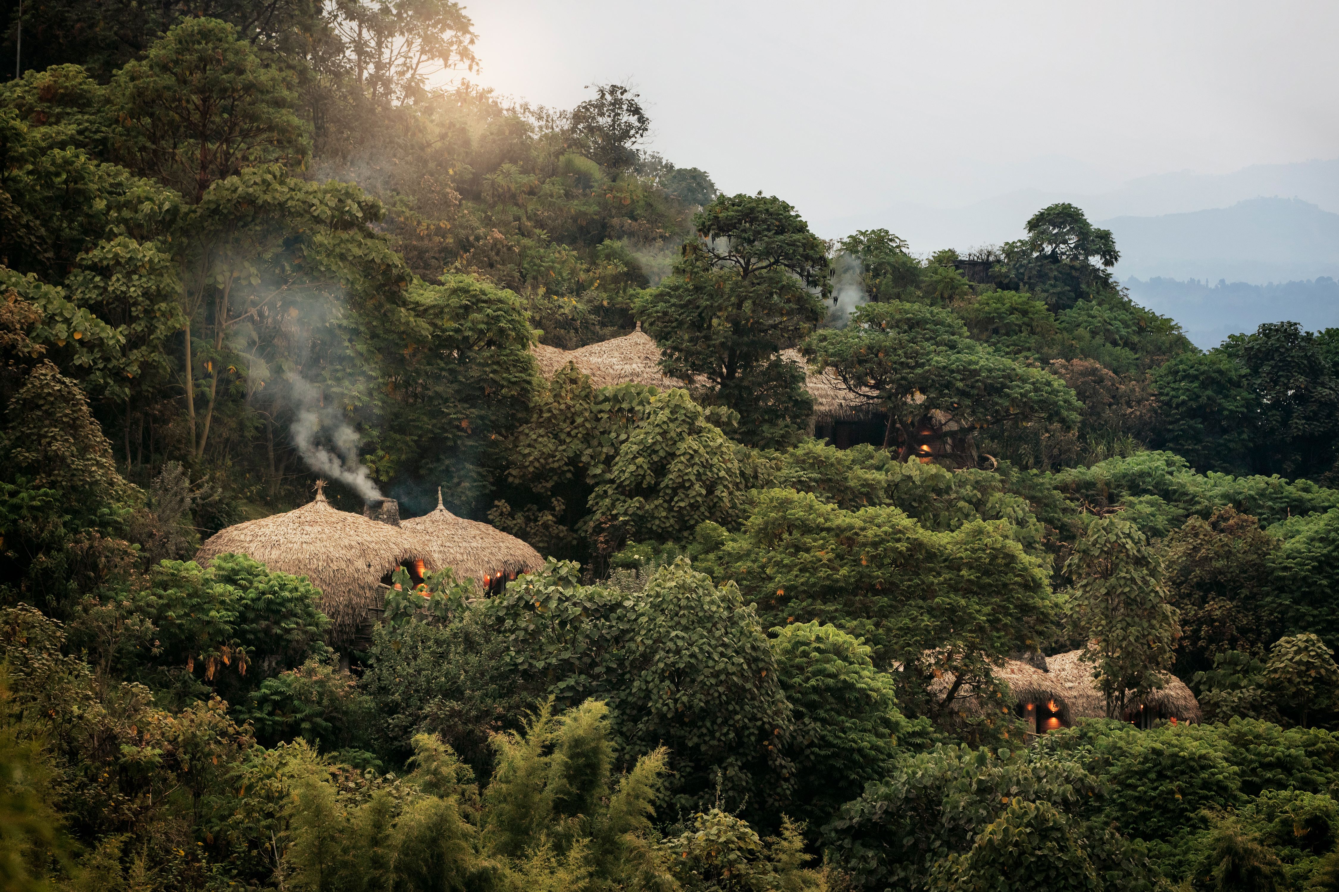 Reetgedeckte Lodges in einer üppig grünen Berglandschaft im warmen Morgenlicht